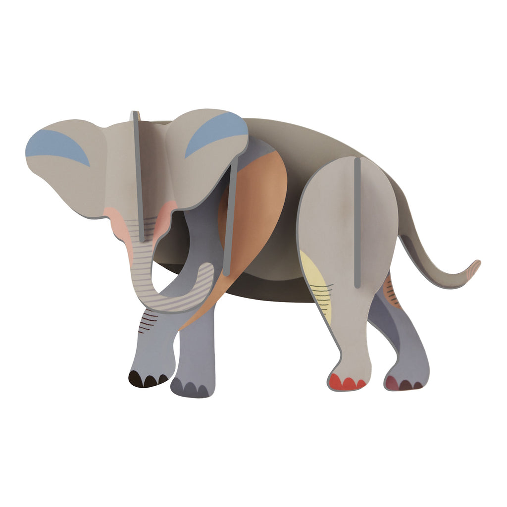 Stylized wooden elephant figurine with pastel colors, including shades of gray, blue, and orange. The design features smooth curves and a playful tone.