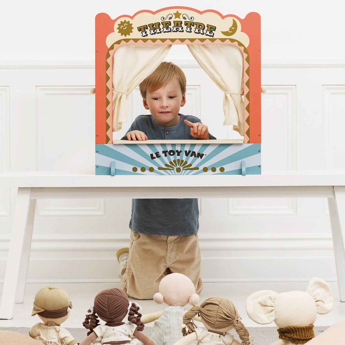 Young boy putting on a show using a wooden tabletop puppet theatre for soft dolls.