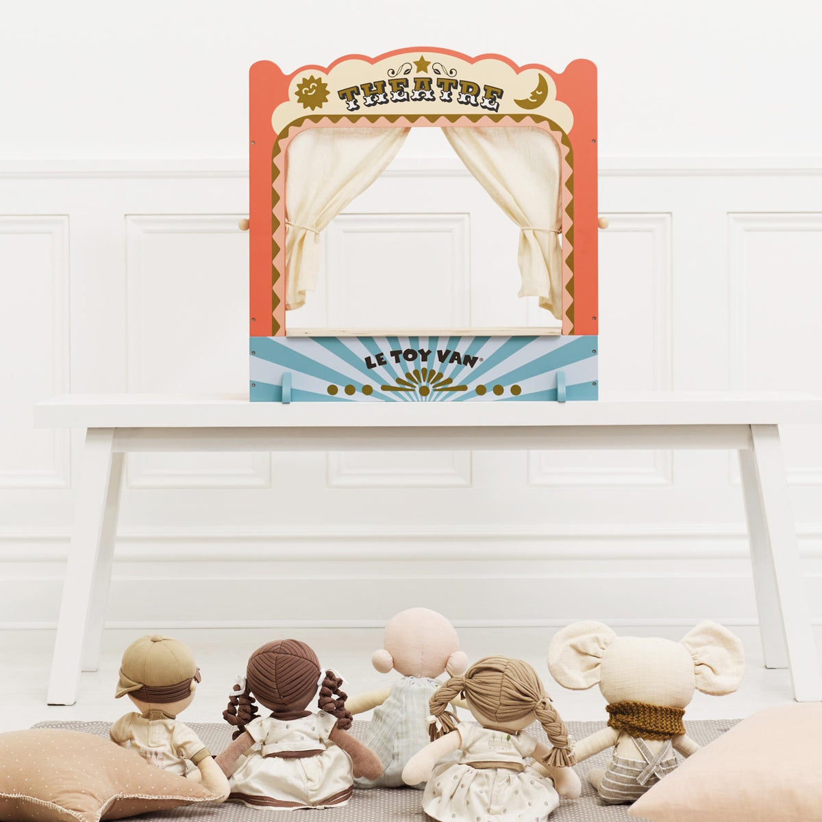 Tabletop wooden puppet theatre set up on a white table with toy dolls seated as the audience.
