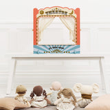 Tabletop wooden puppet theatre set up on a white table with toy dolls seated as the audience.