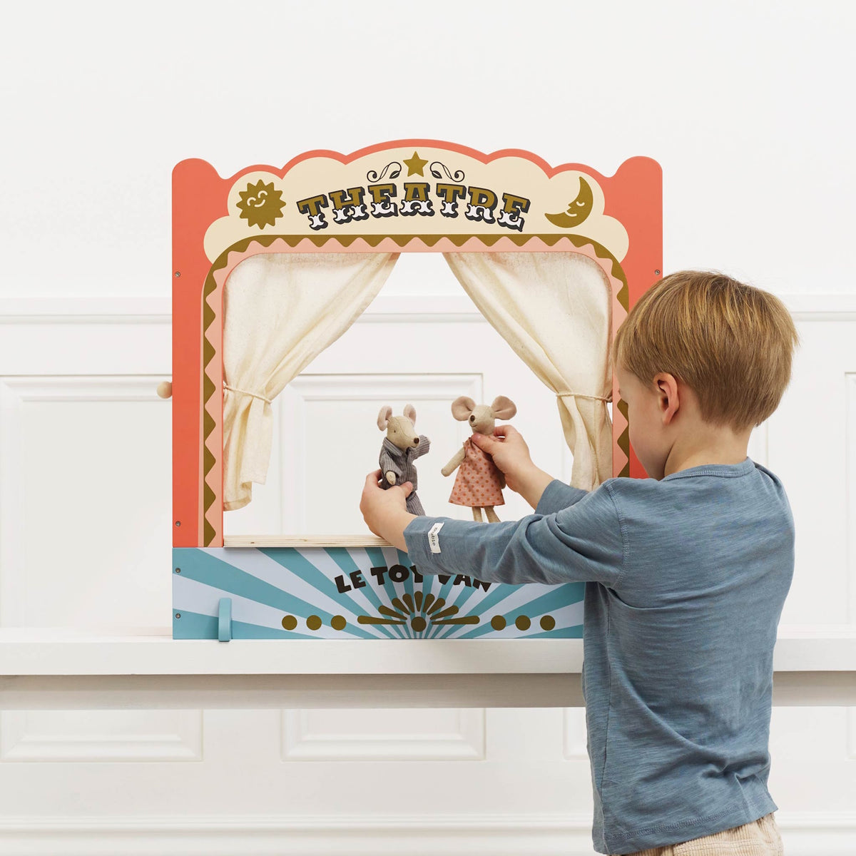 Young boy playing with mouse puppets in a tabletop wooden toy theatre.