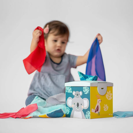 Toddler playing with colorful sensory scarves pulled from a Kimmy Koala Wonder Tissue Box toy.