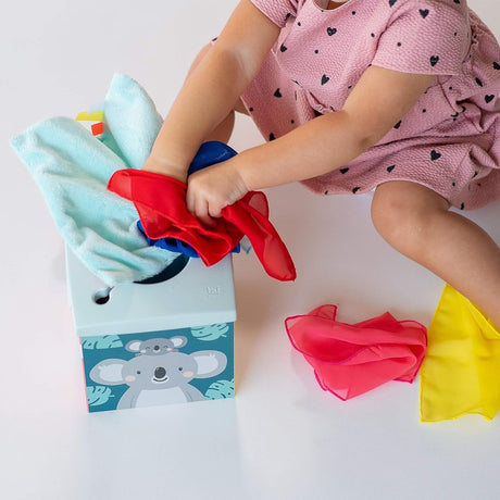 Toddler pulling colorful fabric scarves from a koala-themed sensory tissue box toy.