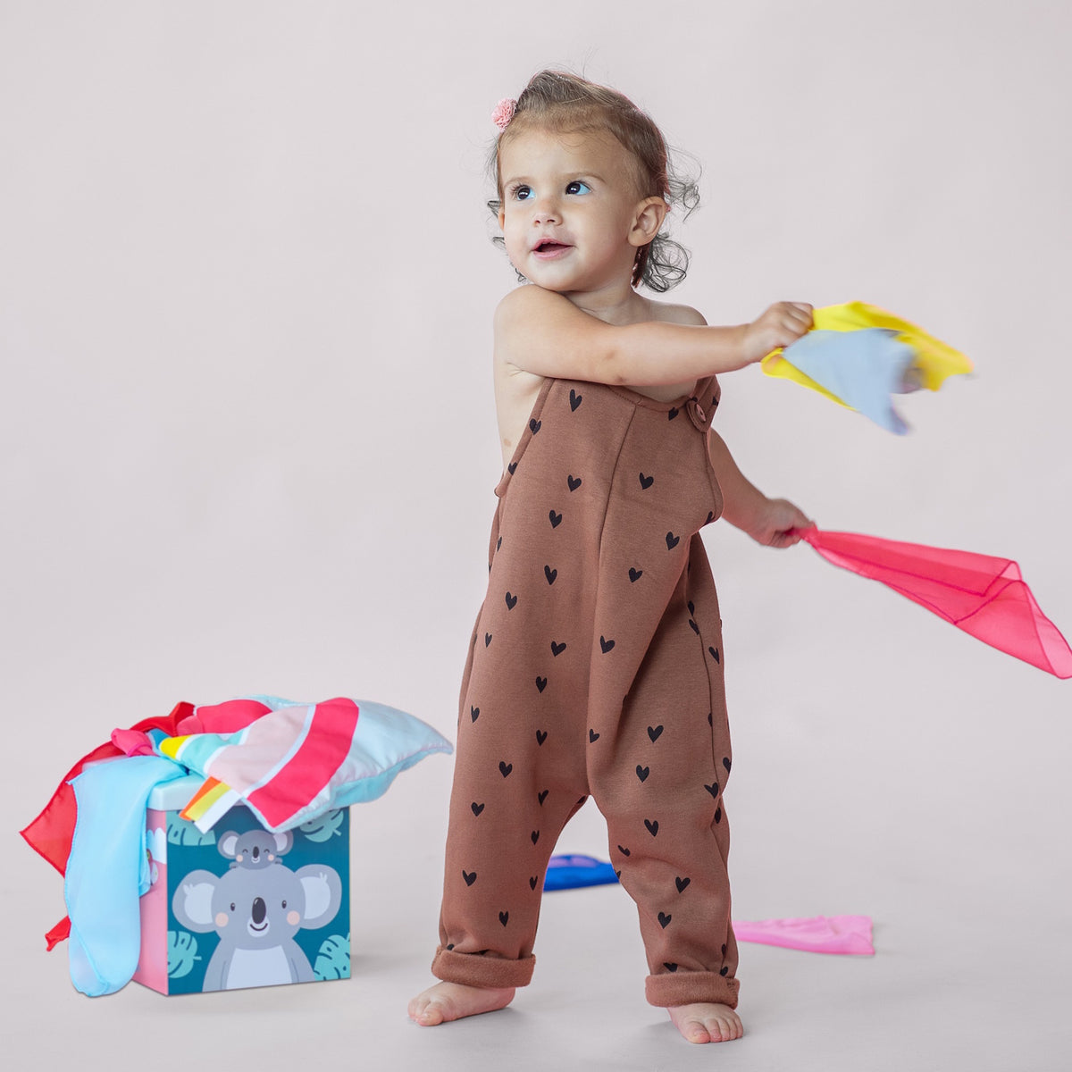 Toddler waving colorful sensory scarves from a Taf Toys Kimmy Koala Wonder Tissue Box play set.