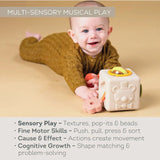 Baby lying on tummy playing with a multi-sensory activity cube toy next to developmental benefit text.