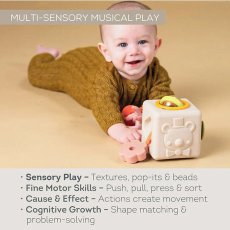 Baby lying on tummy playing with a multi-sensory activity cube toy next to developmental benefit text.
