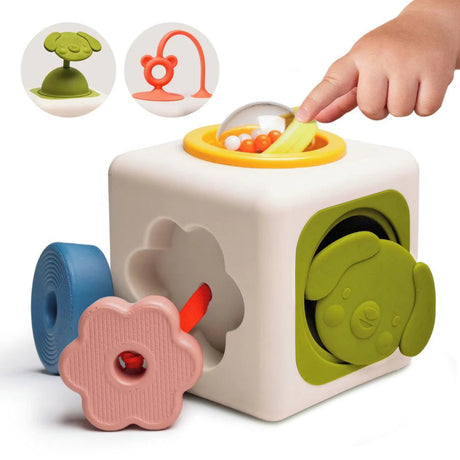 Child's hand spinning a clear rattle ball on top of a sensory activity cube toy with teether and pop-up pieces.