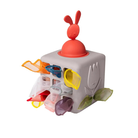 Grey cube activity toy topped with a red bunny pop-up and colorful fabric tissues poking through side slots.