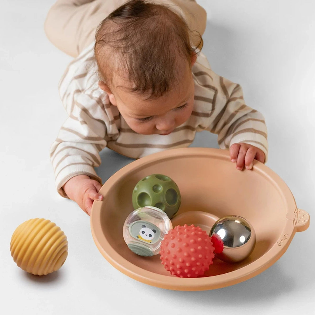 Baby doing tummy time while playing with a tray filled with various textured sensory balls.