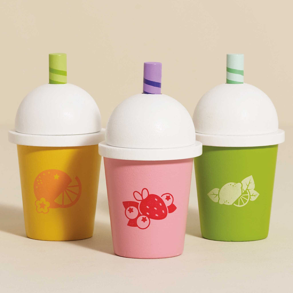 Three colorful cups with white domed lids and striped straws. Each cup has fruit designs: orange on yellow, strawberry on pink, lime on green. Vibrant and playful.