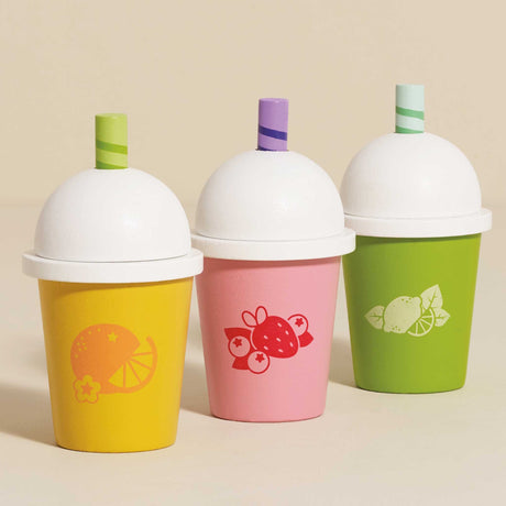 Three wooden play smoothie cups in yellow, pink, and green against a neutral beige background.