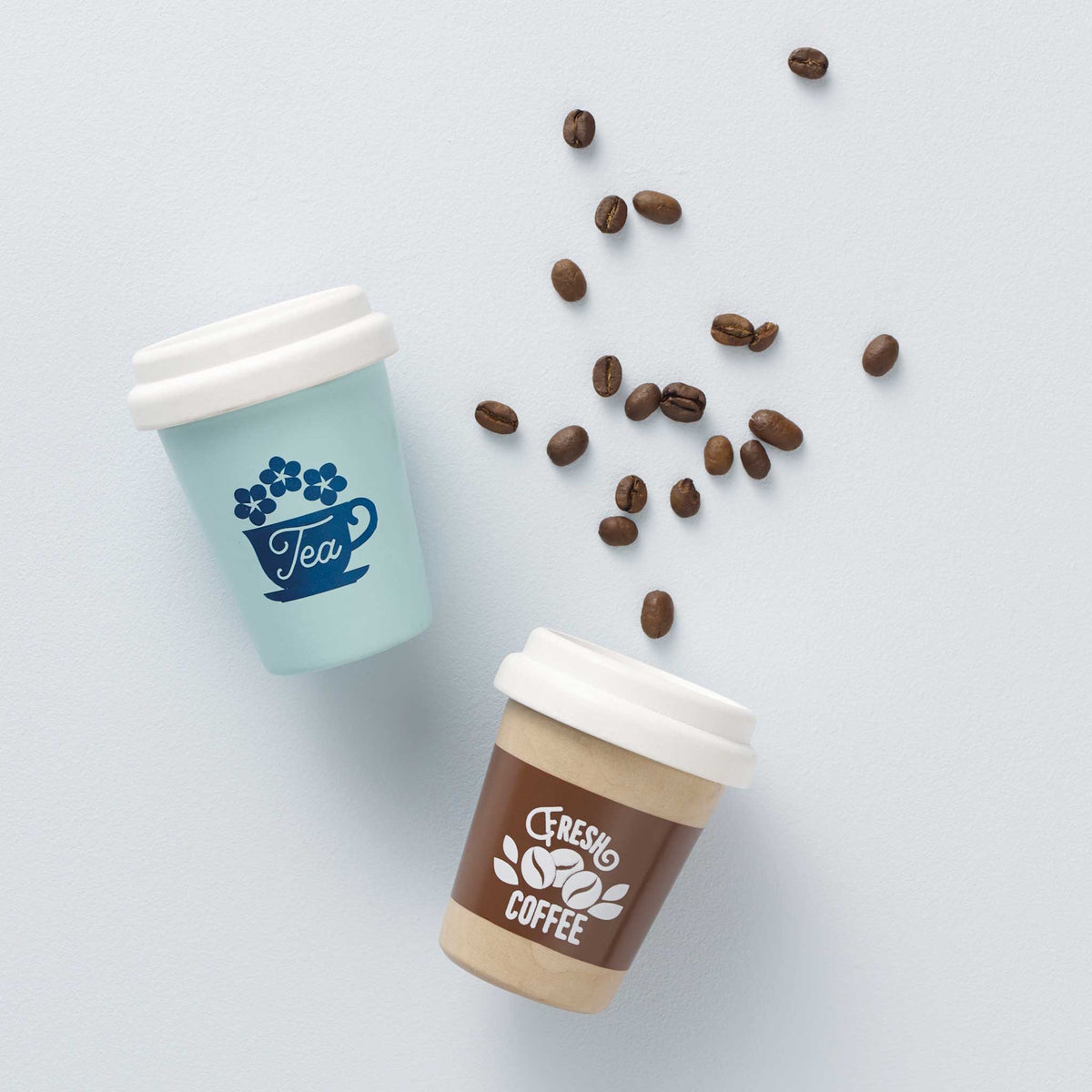 Top-down view of wooden play Tea and Fresh Coffee cups with coffee beans scattered between them.