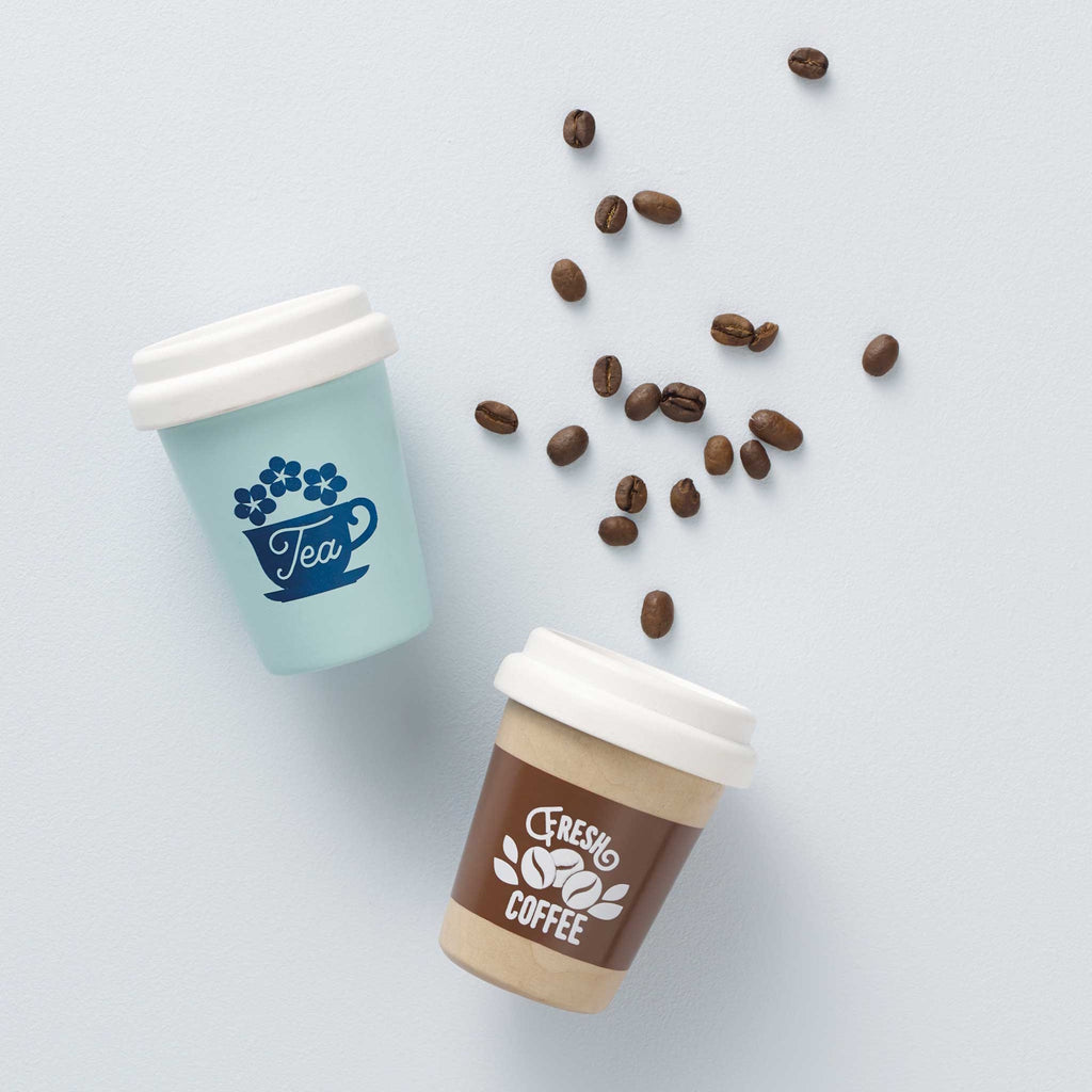 Two small toy cups with white lids: one wooden with "Fresh Coffee" text and beans in brown; the other mint green with "Tea" and a cup design. Playful tone.