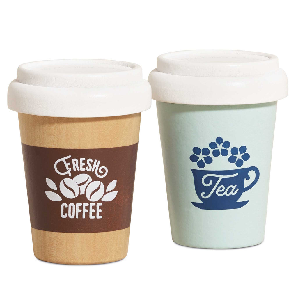 Two small toy cups with white lids: one wooden with "Fresh Coffee" text and beans in brown; the other mint green with "Tea" and a cup design. Playful tone.