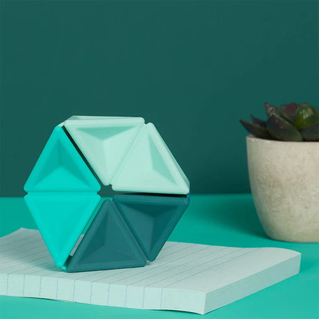 Teal silicone hexaflexagon fidget toy upright on a notepad next to a potted succulent.