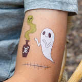 Child's arm with temporary tattoos of a ghost, a poison bottle with green smoke, and stitches.
