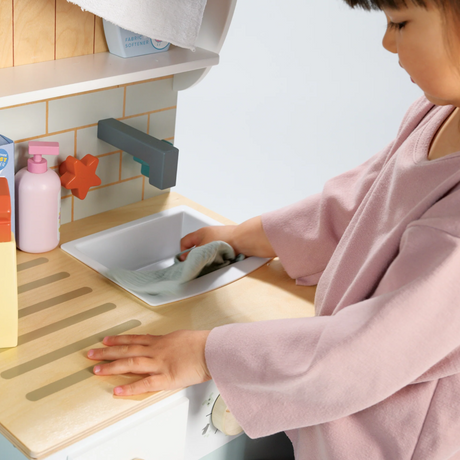 Child washing a play cloth in the sink of a wooden toy laundrette.
