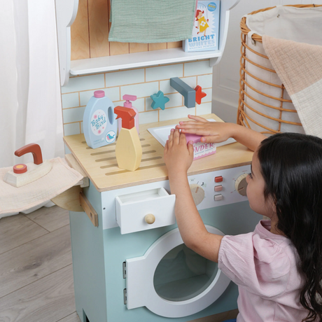 Child pressing down on wooden laundry detergent box at a play laundrette set.