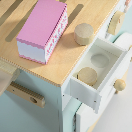 Close-up of an open wooden detergent drawer with play laundry tablets next to a pink box.