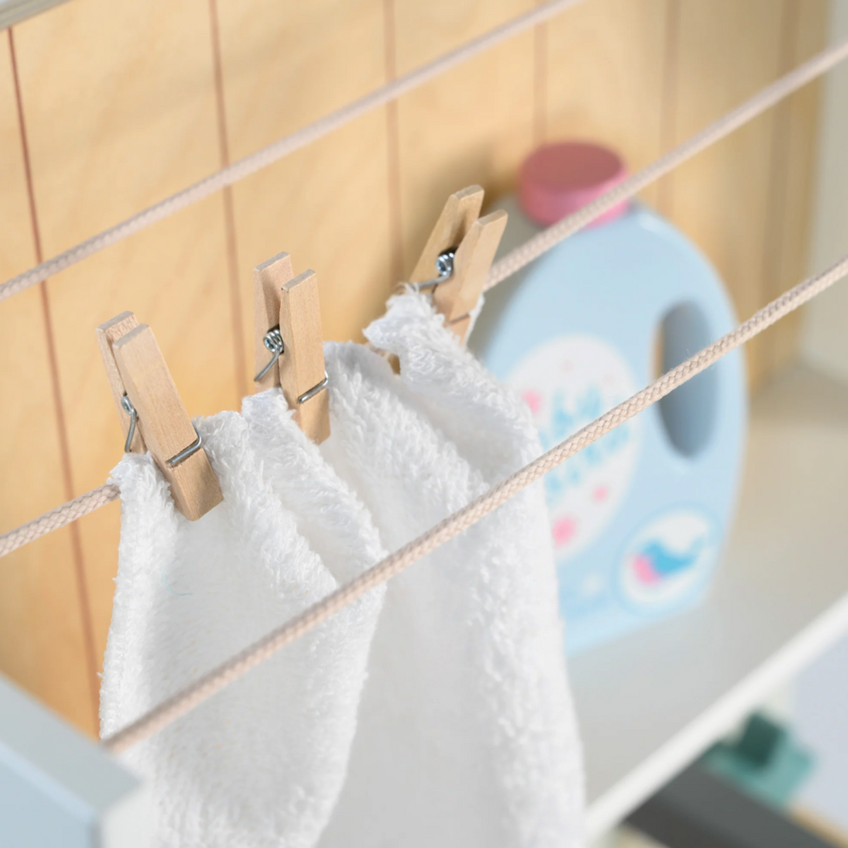 Close-up of an open wooden detergent drawer with play laundry tablets next to a pink box.