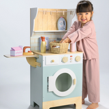 Young girl in pink pajamas playing with a wooden toy laundrette set.