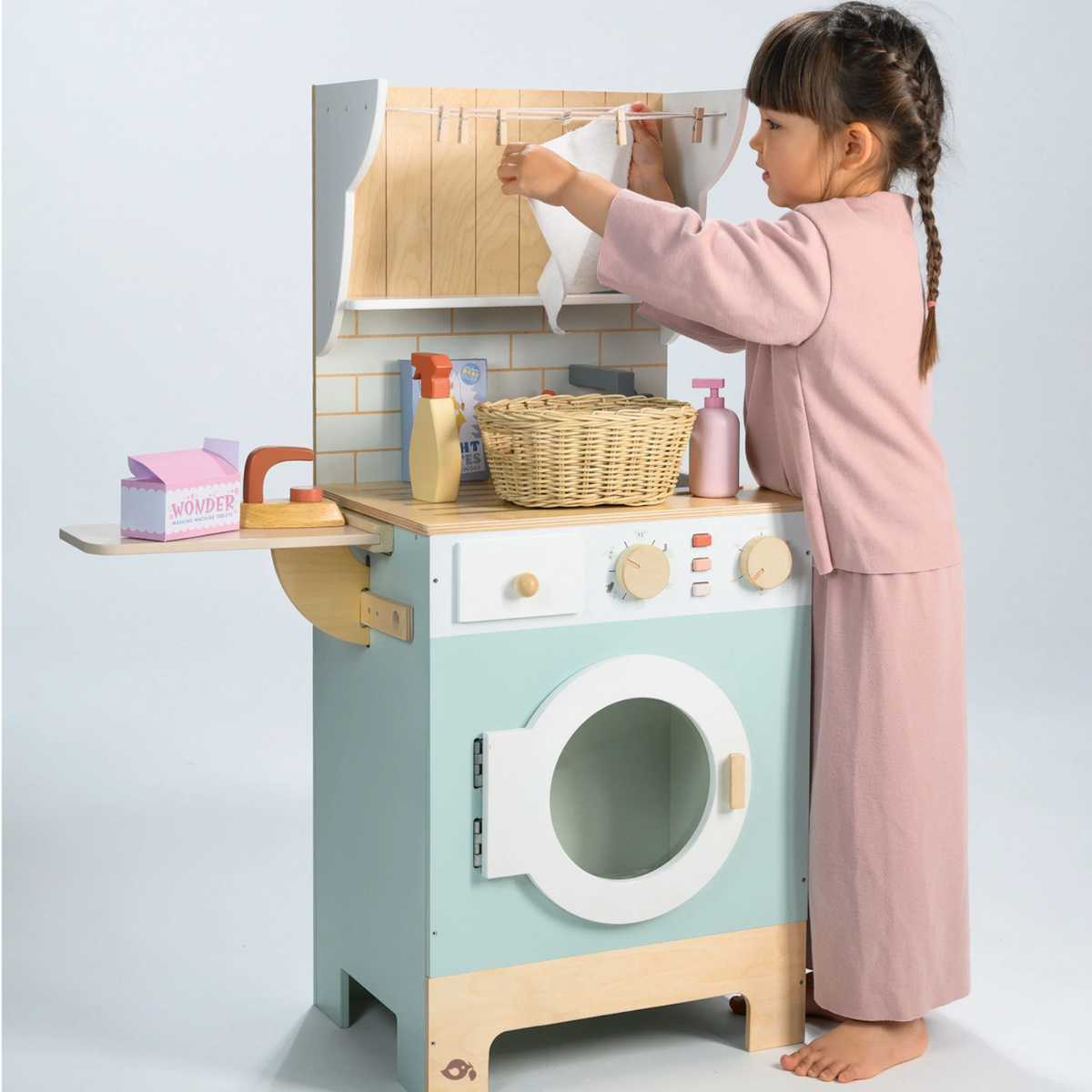 Little girl hanging play laundry on the clothesline of a wooden toy laundrette.