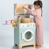 Little girl hanging play laundry on the clothesline of a wooden toy laundrette.