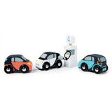 Three toy cars in orange, white, and blue, with the white car plugged into an EV charging station.