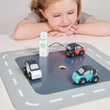 A young girl happily plays with a wooden toy car set on a road mat.