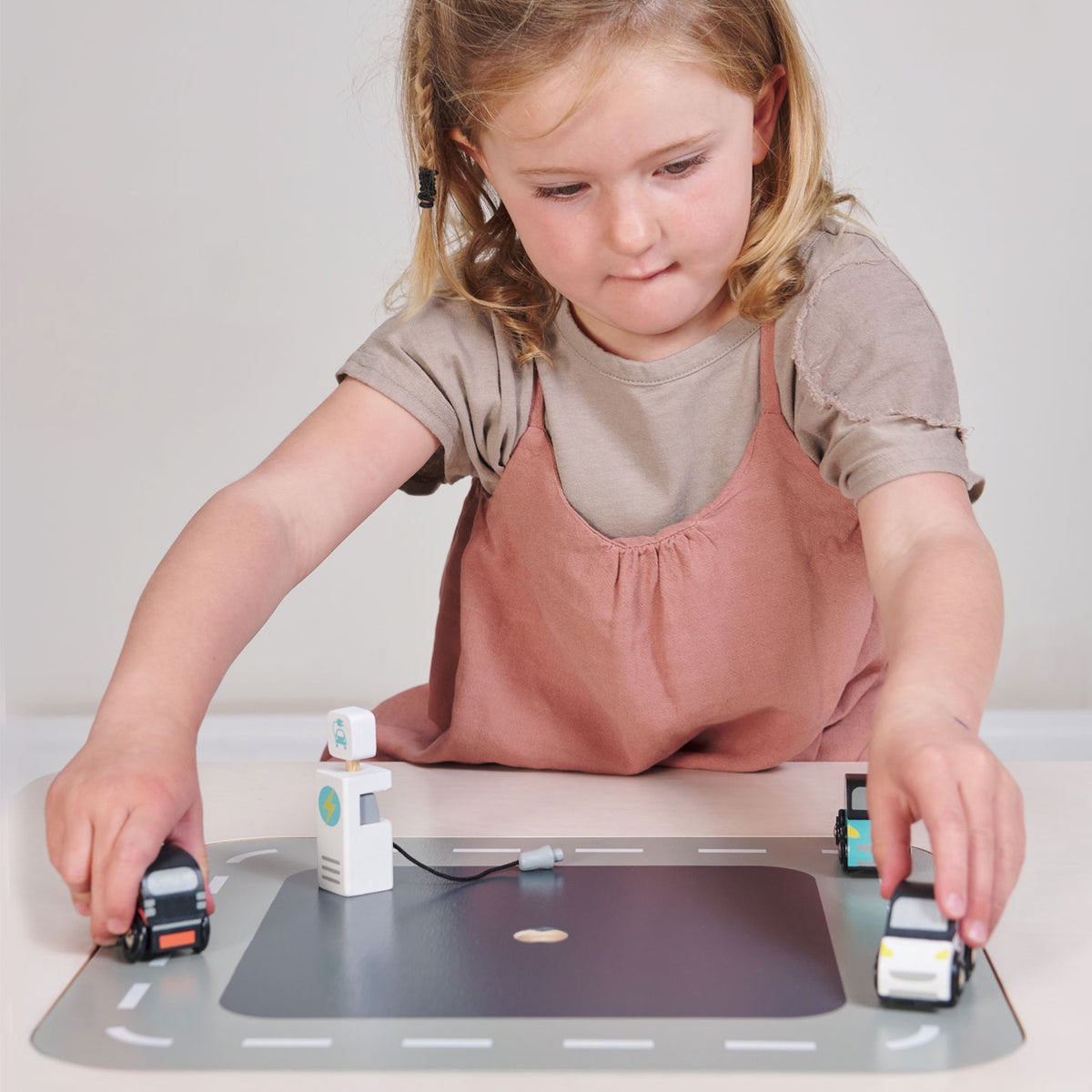 A young girl playing with a wooden car set on a road mat.