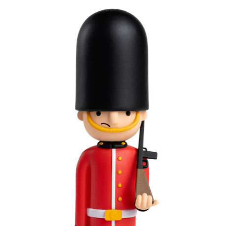 Toy soldier figurine with a British guard uniform, featuring a tall black hat and red coat, holding a rifle. The backdrop is solid white.