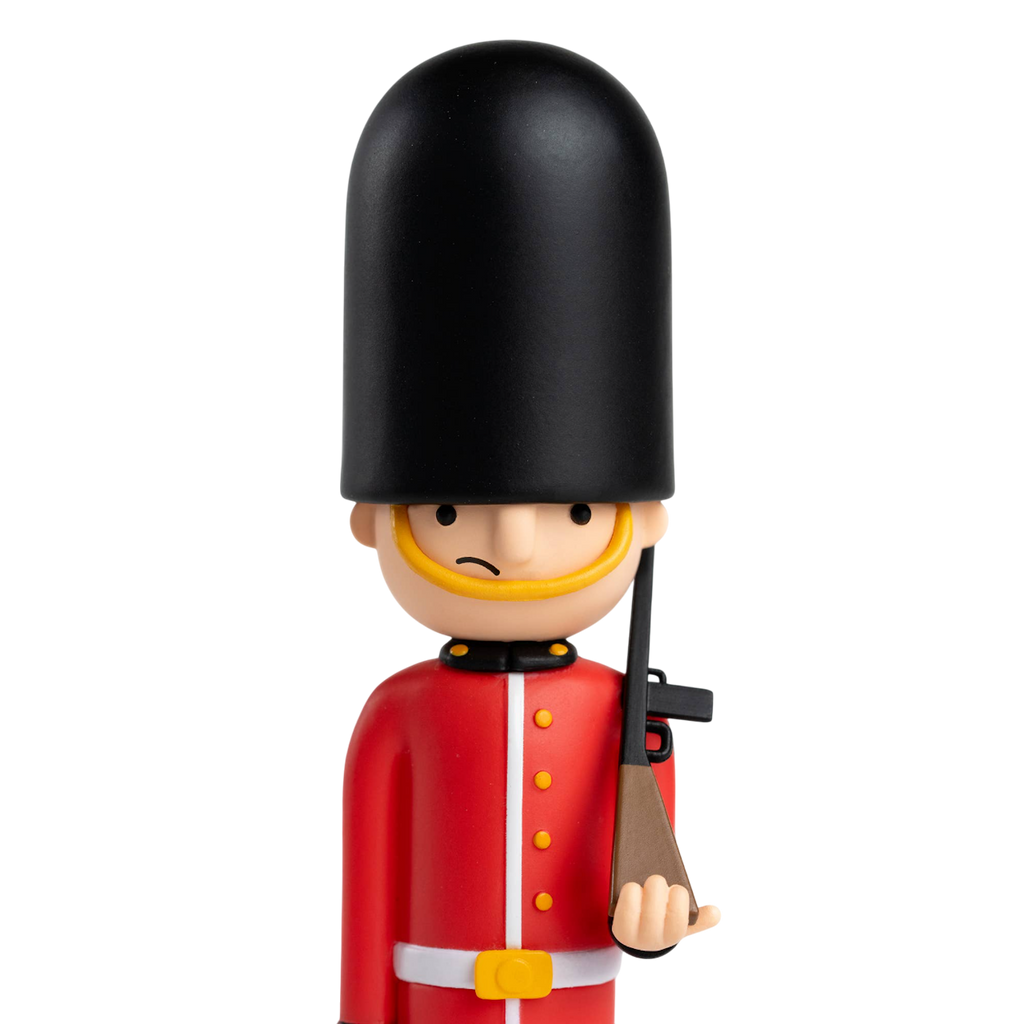 Toy soldier figurine with a British guard uniform, featuring a tall black hat and red coat, holding a rifle. The backdrop is solid white.