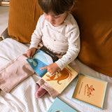 Young child sitting on a bed pointing at illustrations in a fabric rag book.