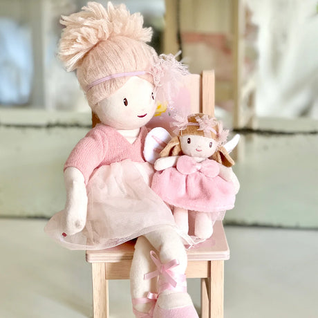 Large rag doll in a pink tutu sitting on a wooden chair holding a small plush fairy doll.