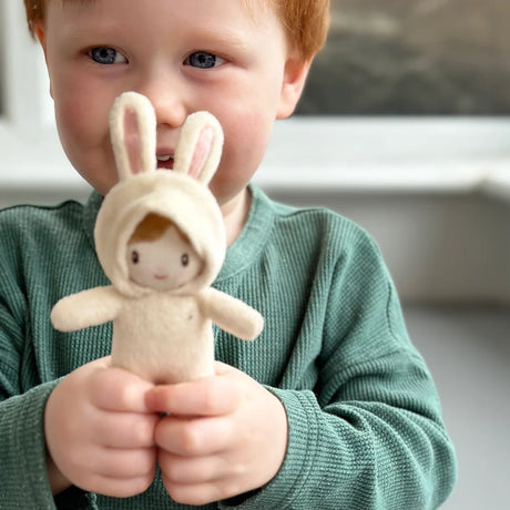 A young child with red hair holding a tiny plush toy wearing a cream bunny costume.