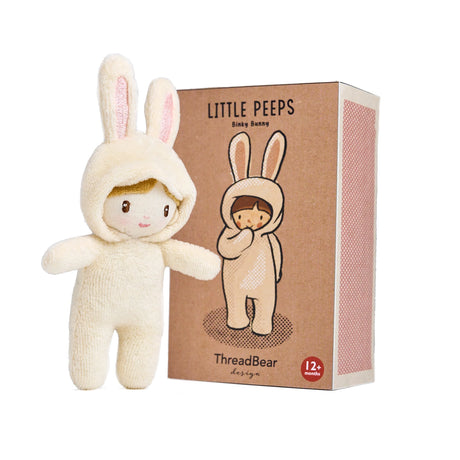 Small plush doll in a cream bunny suit standing next to its Little Peeps Binky Bunny box.