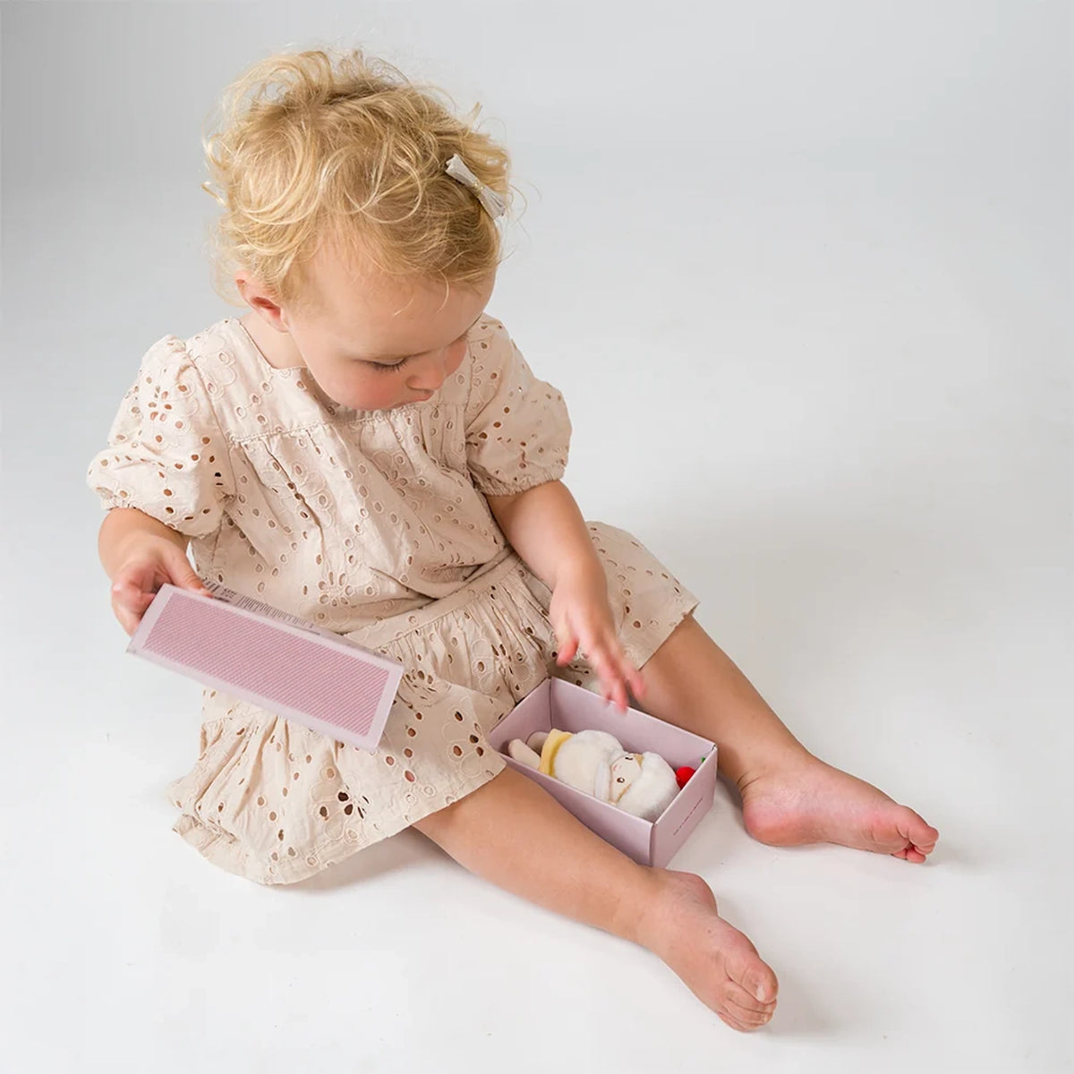 Toddler sitting on the floor opening a small pink box containing a plush doll.