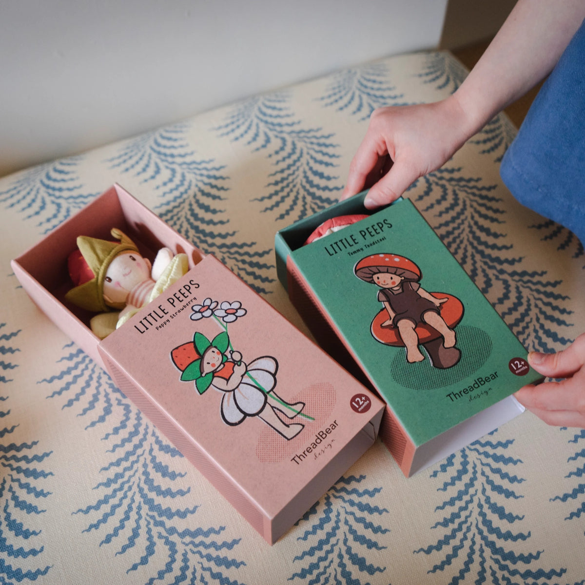 Person opening matchbox-style boxes for "Poppy Strawberry" and "Tommy Toadstool" plush dolls.