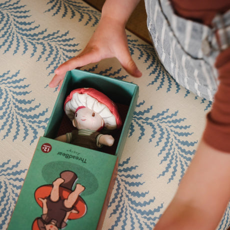 Child opening a green illustrated box to reveal a small toadstool plush doll inside.
