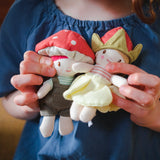 Child's hands holding two small plush dolls, one with a toadstool hat and one with a strawberry hat.