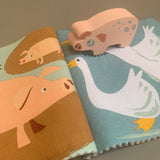 Wooden pig toy standing on an open cloth book illustrating pigs and geese.