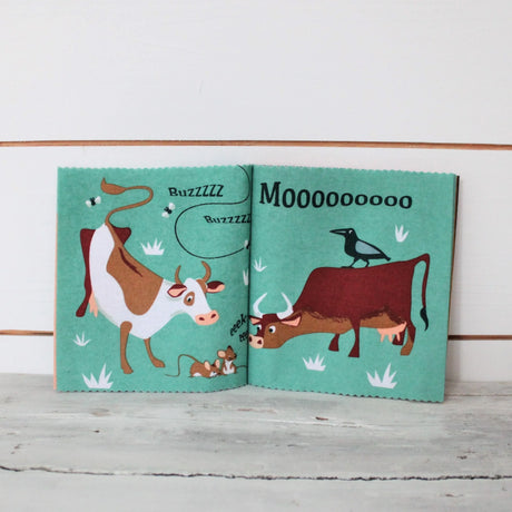 Open fabric book showing cows, mice, flies, and a bird on teal pages.