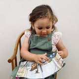 Child sitting in a wooden chair reading an illustrated fabric book about forest animals.