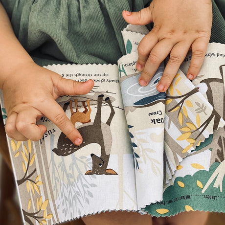 Toddler's hands pointing to a deer illustration in a soft cloth book.