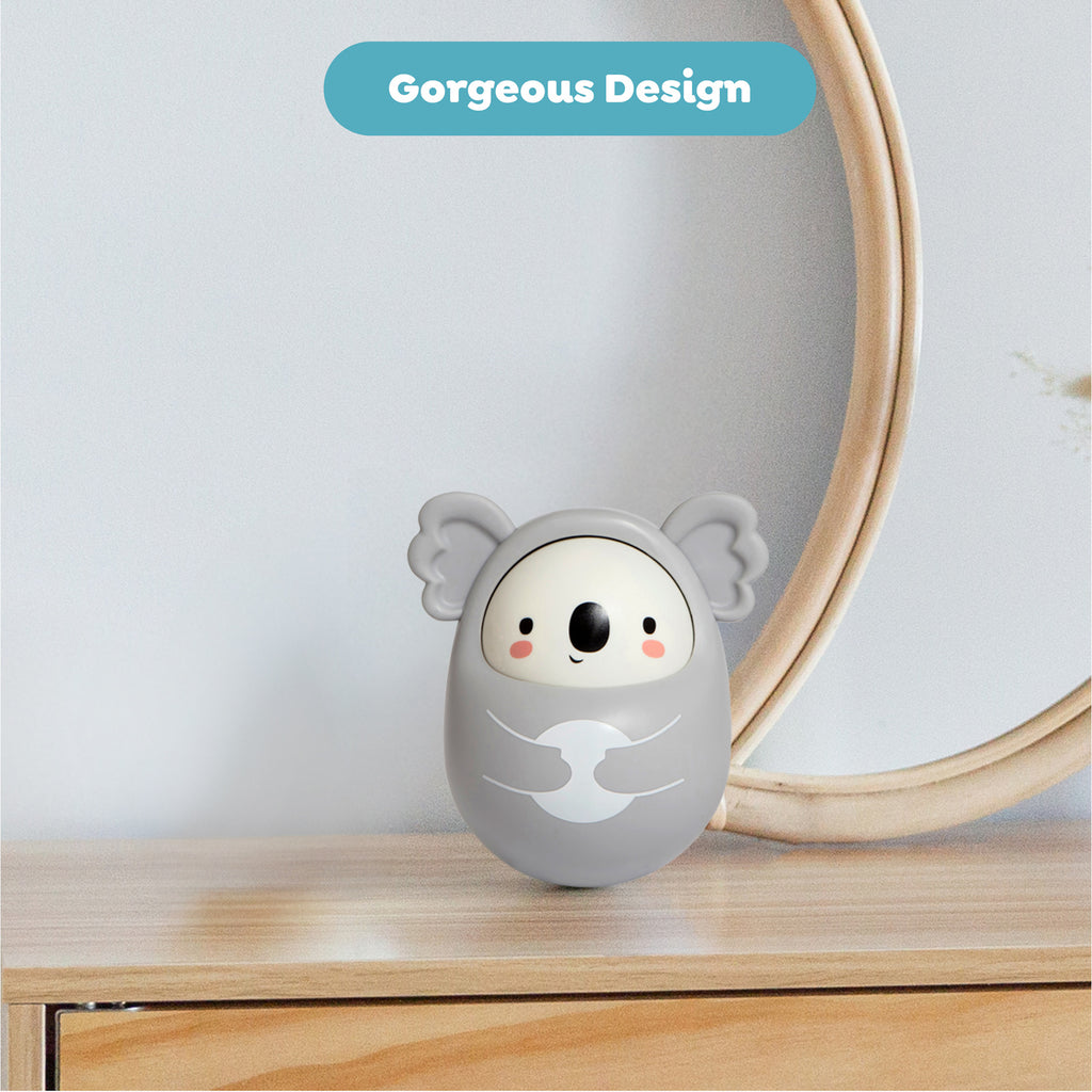 Cute koala-shaped gray toy with a smiling face, sitting on a wooden table. Above, a blue label reads "Gorgeous Design," creating a playful tone.
