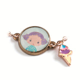 A children's bracelet from Djeco's Tinyly collection featuring a gold-colored chain and a pendant of Tutti, a character depicted with an ice cream accessory.