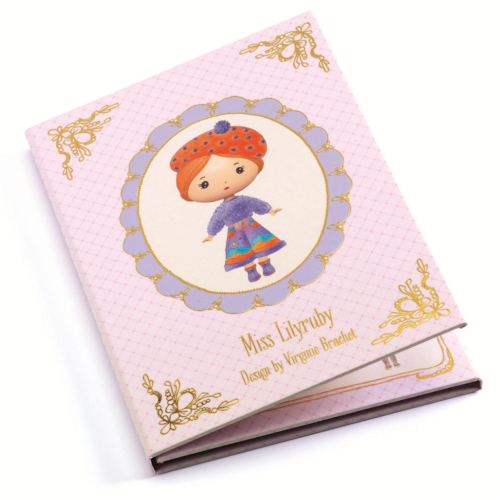 The set includes a fold-out booklet with a central illustration of Miss Lilyruby and four sheets of reusable vinyl stickers, allowing children to dress and accessorize her in various outfits.