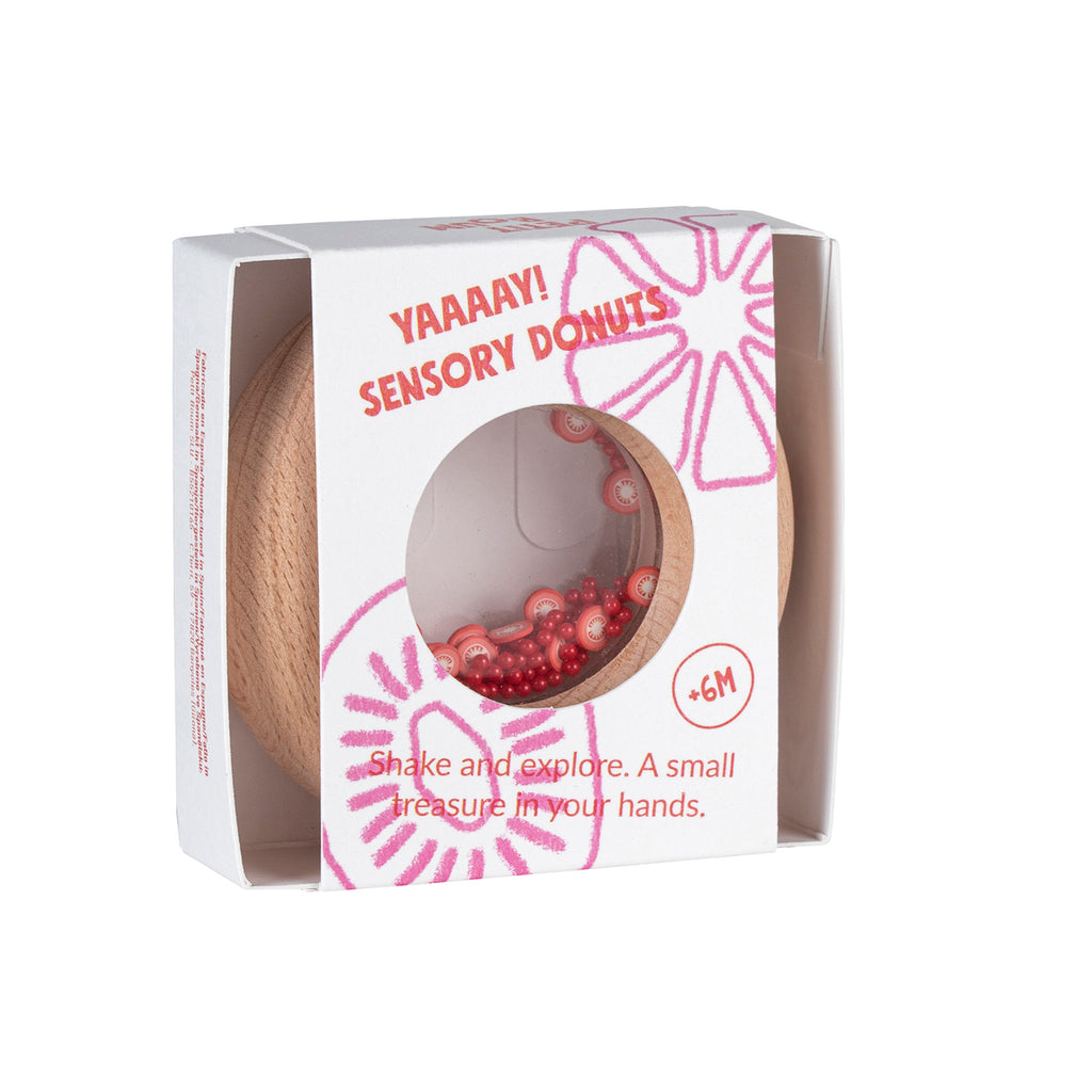 A Petit Boum tomato-themed wooden sensory donut in its packaging, featuring red and white tomato slices inside a clear window.