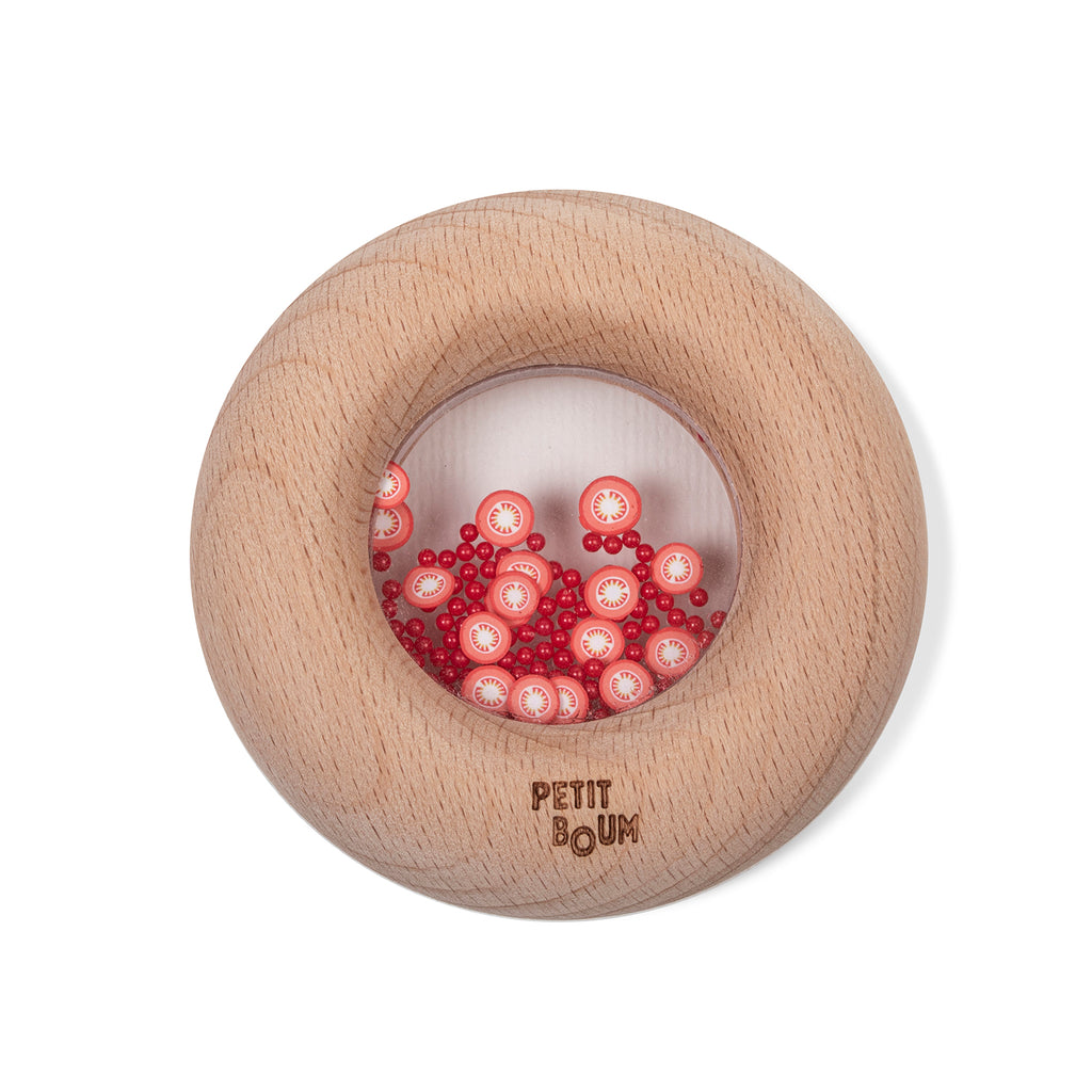 A round wooden sensory toy with a clear window, filled with tiny red and white tomato slice decorations.