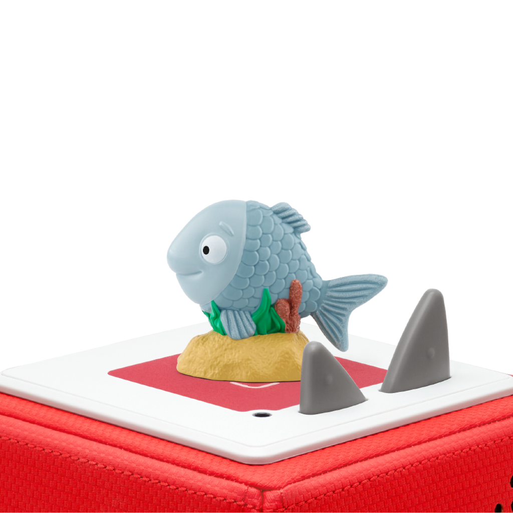 A whimsical blue fish figurine with detailed scales is perched on a sandy base atop a red box. Two gray, fin-like shapes protrude from the box.